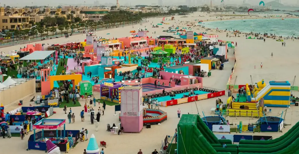 Aerial view of the colourful Beach Canteen food and entertainment festival on a Dubai beach, with stalls, inflatables and crowds by the sea — powered by Glow Power Rental