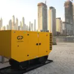 Row of yellow Glow Power Rental GP diesel generators on a Dubai beach providing emergency standby power, with the Dubai Marina skyline and Ain Dubai behind
